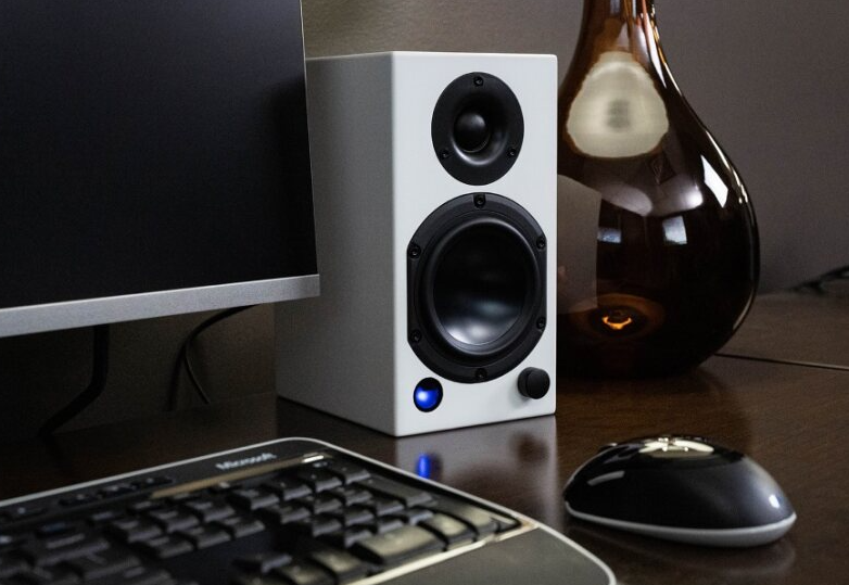 Lifestyle image of the M-Series white speaker next to a computer monitor