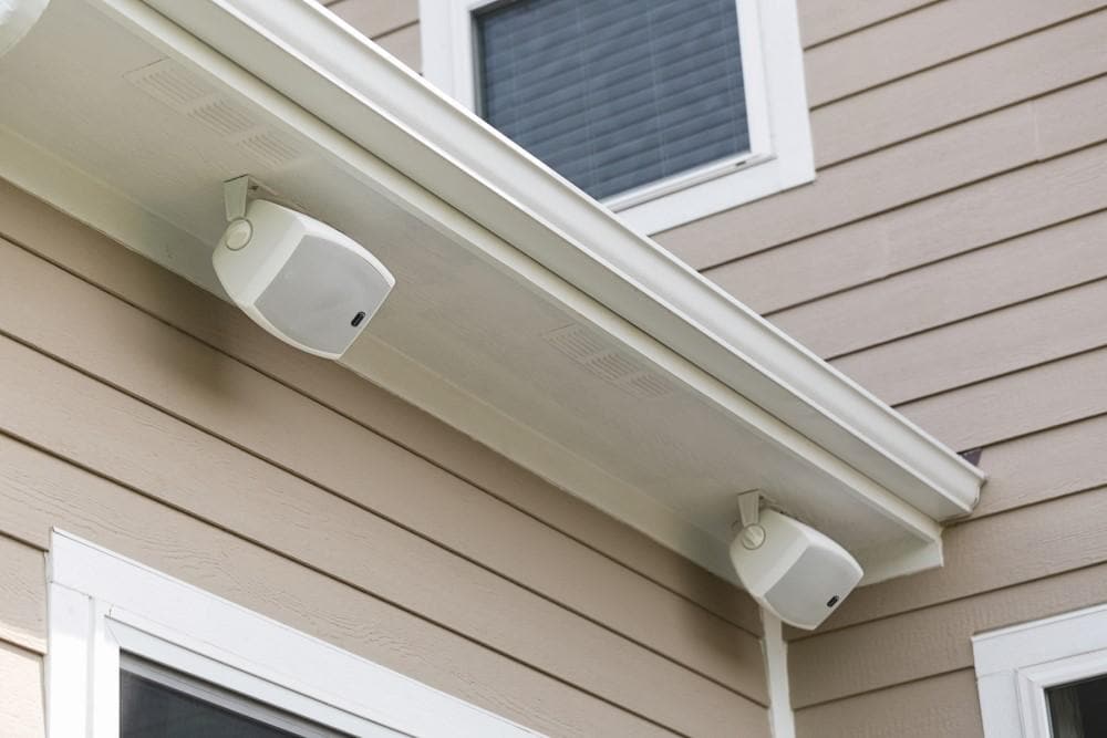 Dayton Audio IO Series speakers mounted under the lip of a house roof.